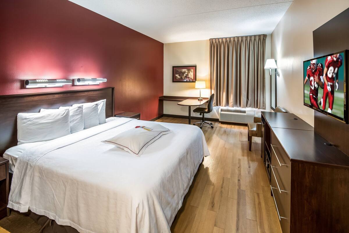 Una habitación de hotel con una cama grande, un escritorio, una silla, un televisor y una ventana con cortinas.