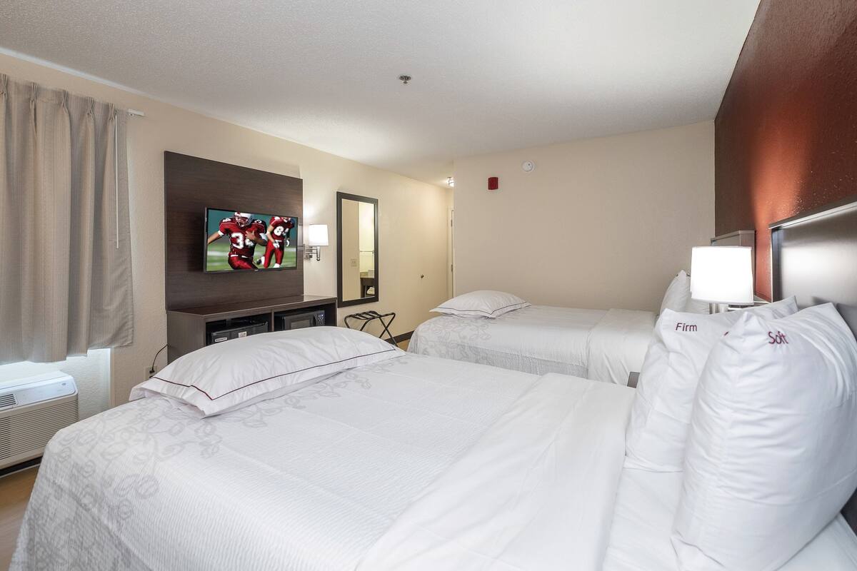 Habitación de hotel con dos camas, televisor, escritorio y espejo.