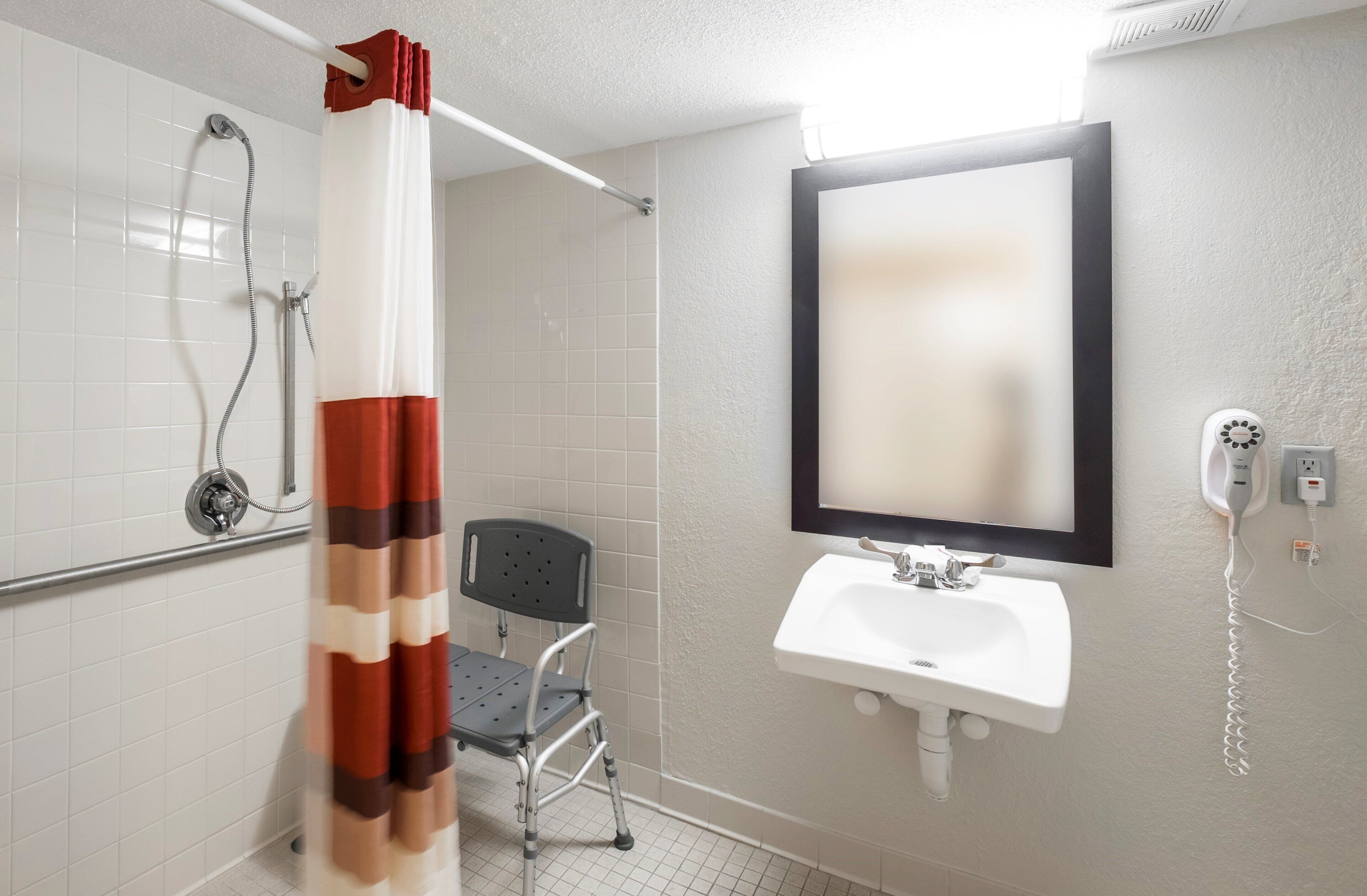Un baño con ducha, lavamanos, una silla y un espejo.