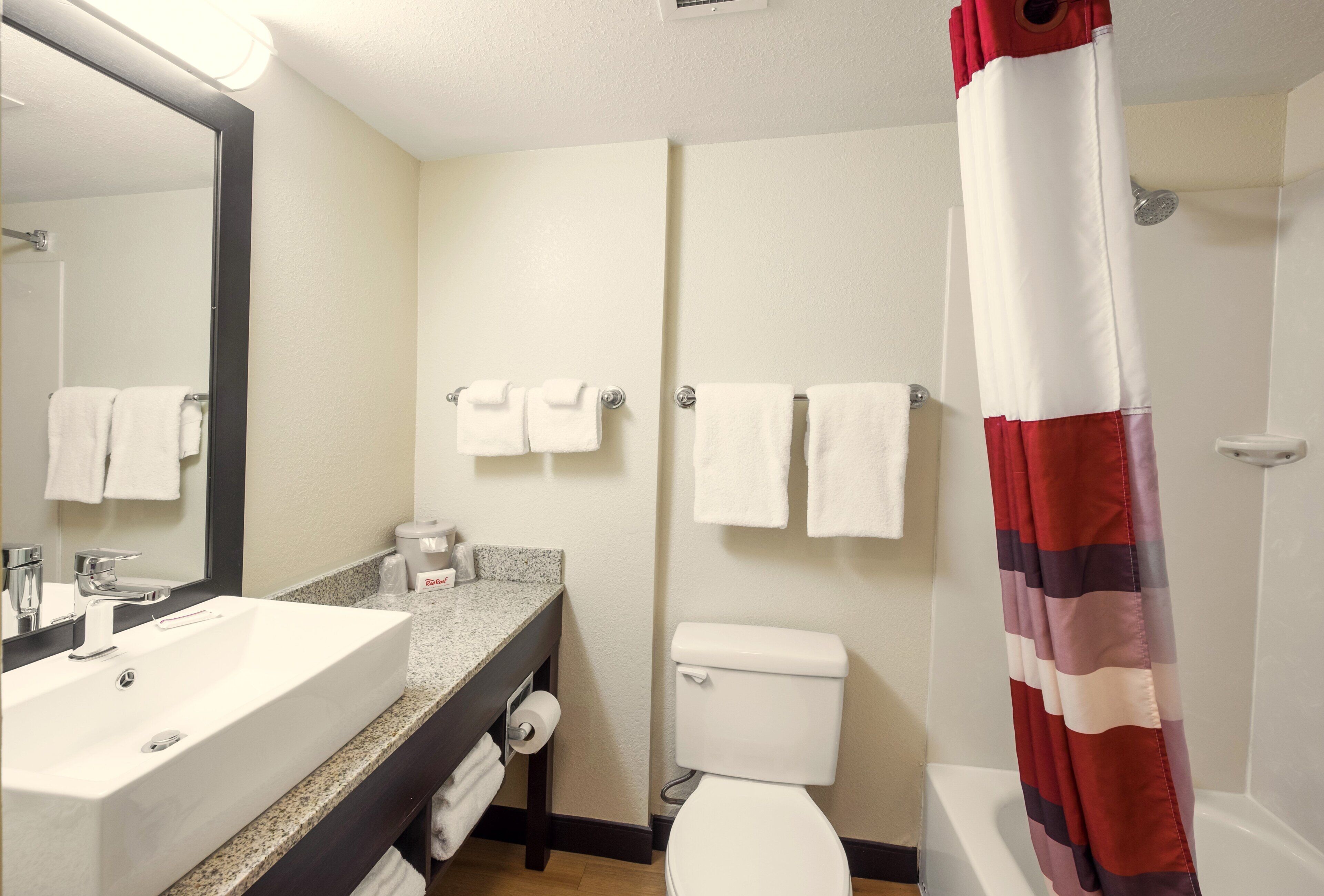 A bathroom with a sink, toilet, and shower. There are towels hanging on the wall.
