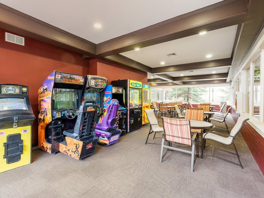 Un espacio de juegos con máquinas de arcade, una zona de estar con mesas y sillas, y ventanas amplias que dejan entrar luz natural.