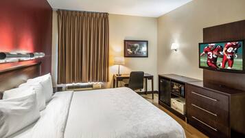 Quarto de hotel com cama grande, escrivaninha, cadeira, televisão e minibar.
