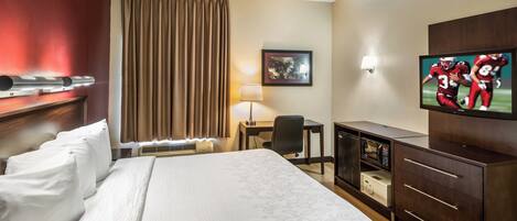 Una habitación de hotel con una cama grande, un escritorio, una silla, un televisor y un mini bar.