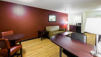 A hotel room with a dining table, two chairs, a sofa, a small table, a lamp, and a kitchenette.