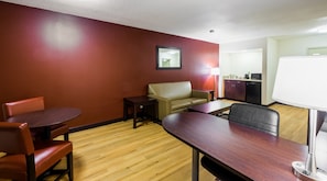A hotel room with a dining table, two chairs, a sofa, a small table, a lamp, and a kitchenette. - Red Roof Inn PLUS+ South Deerfield – Amherst (South Deerfield)