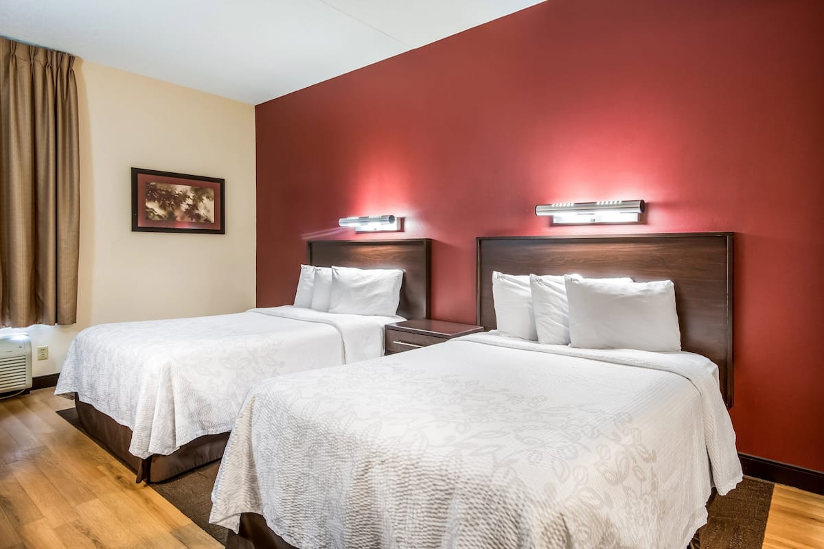 Una habitación de hotel con dos camas, una pared de acento roja y un cuadro enmarcado en la pared.