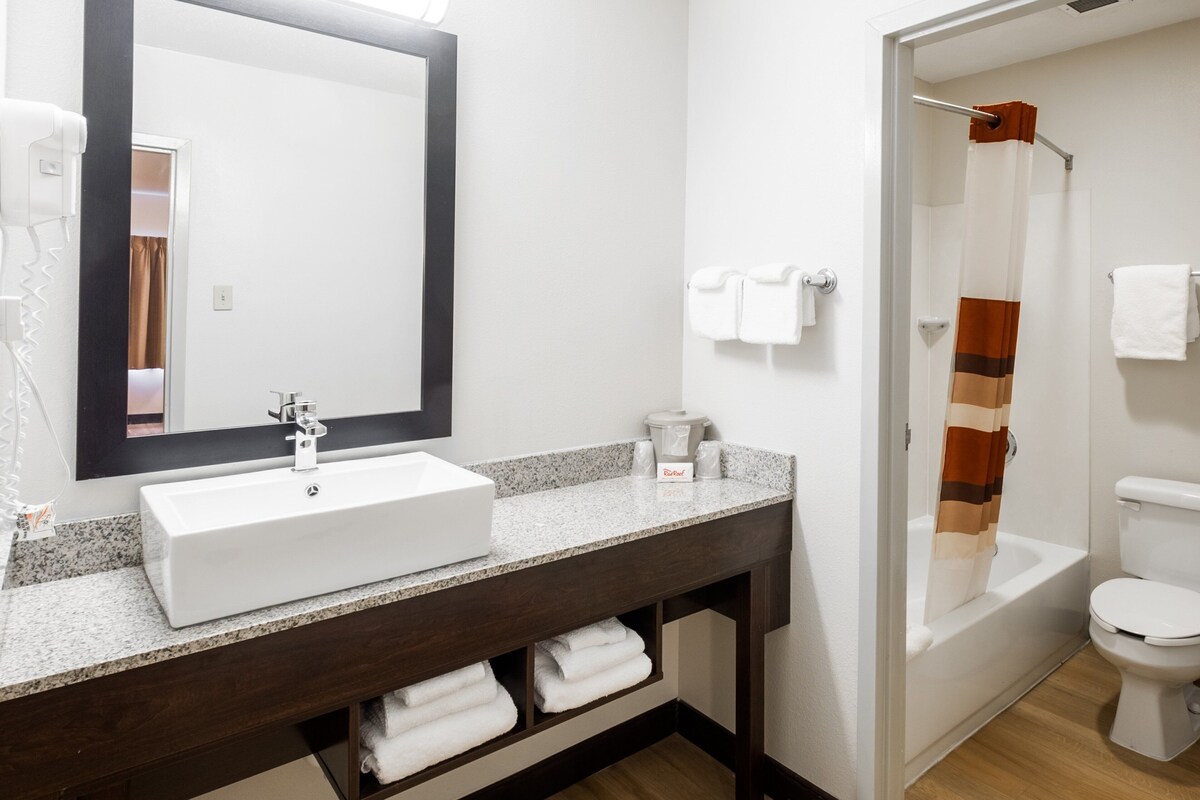 A bathroom with a white sink, dark wooden vanity, a large mirror, a shower curtain, and a toilet.