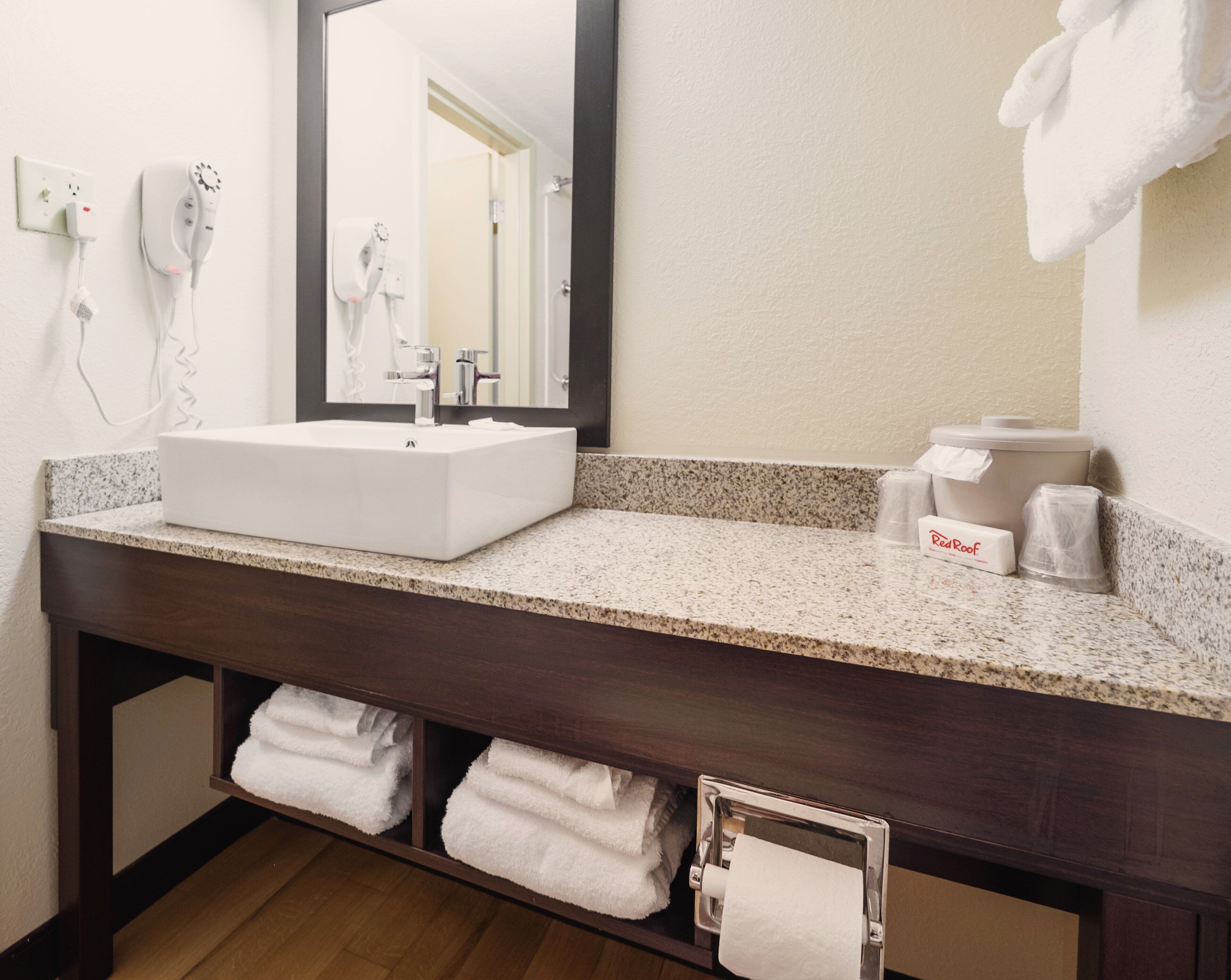 A hotel bathroom with a white sink, a mirror, a towel rack, and a Red Roof tissue box.