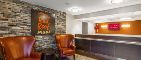 A hotel reception area with a stone wall, leather chairs, a reception desk, and a sign indicating free Wi-Fi.
