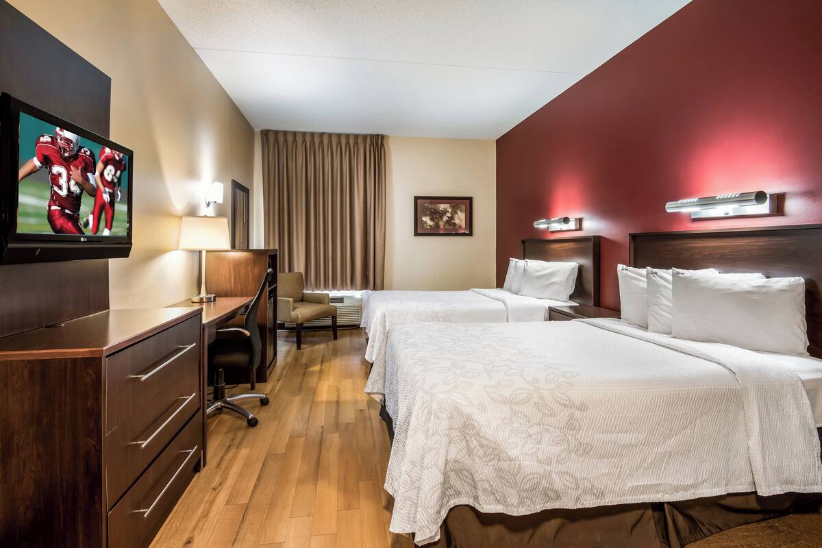 Habitación de hotel con dos camas, un escritorio, una silla, un televisor y una lámpara.
