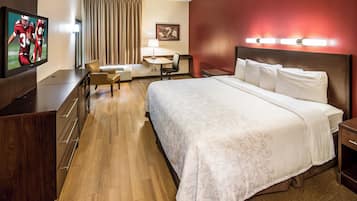 Habitación de hotel con cama, escritorio, silla, televisor y lámpara.