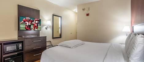Habitación de hotel con cama, televisión, espejo, escritorio con microondas y lámpara.