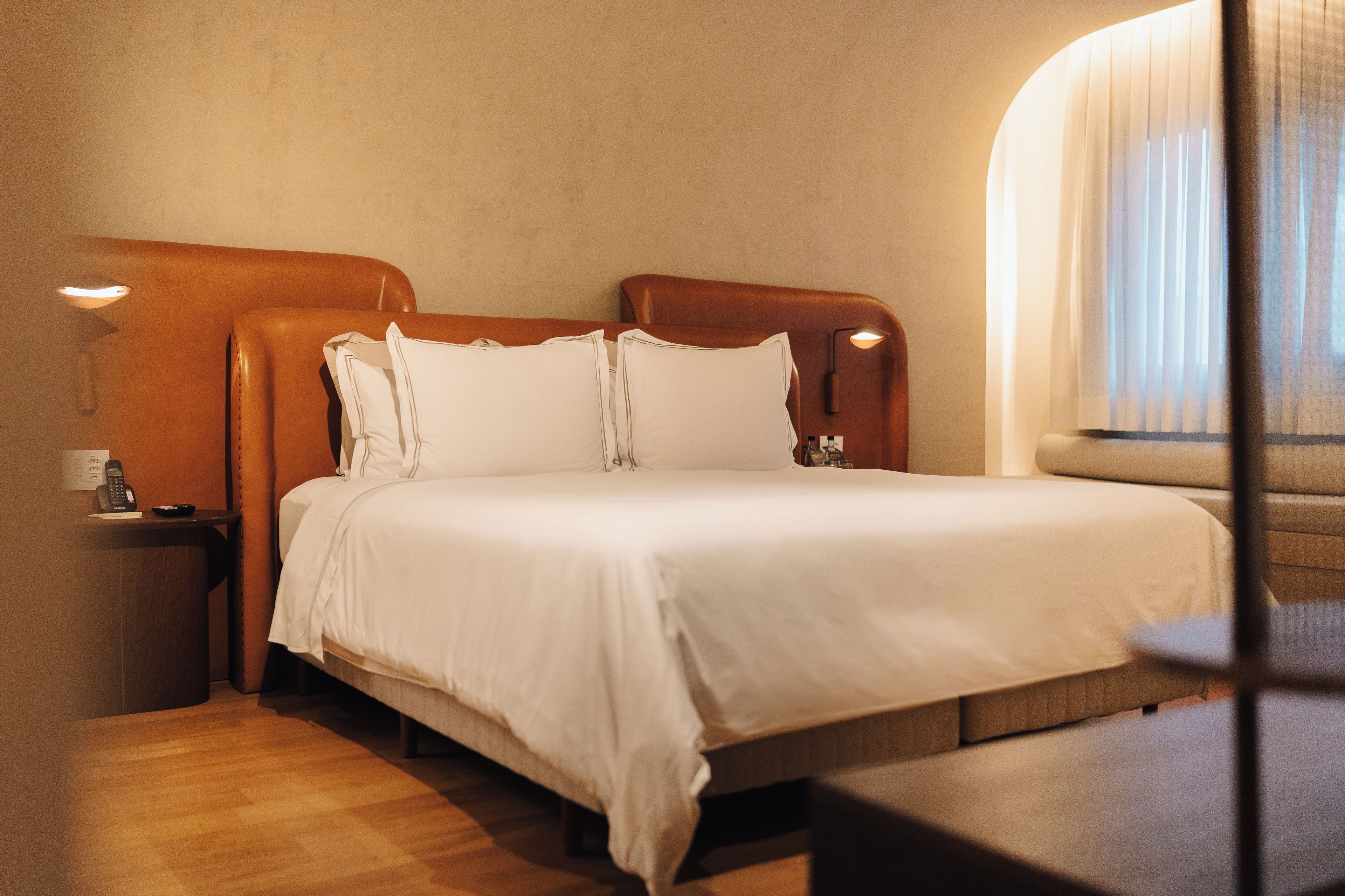Una habitación de hotel con una cama grande, una mesita de noche, una lámpara y una ventana con cortinas.