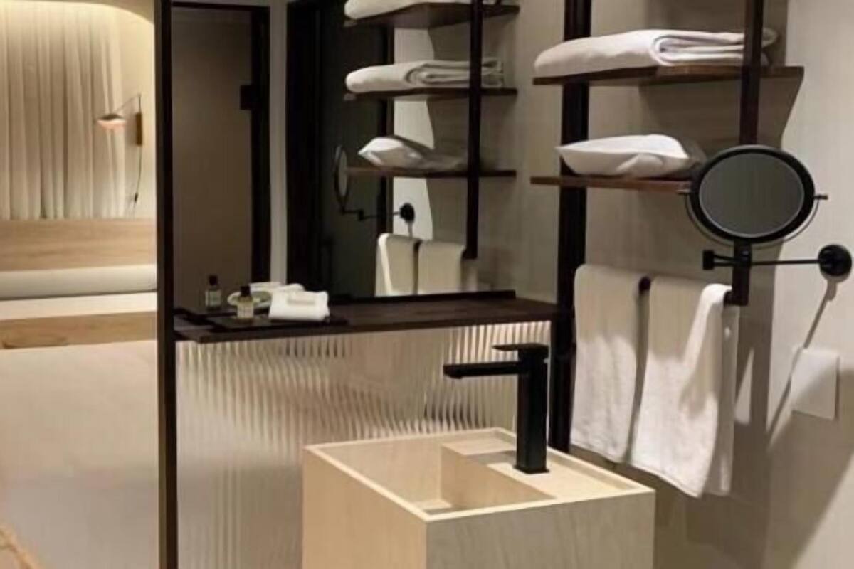 Une chambre d’hôtel moderne équipée d’un lit, d’un petit coin salon, d’un bureau, d’un miroir rond et d’un lavabo intégré.