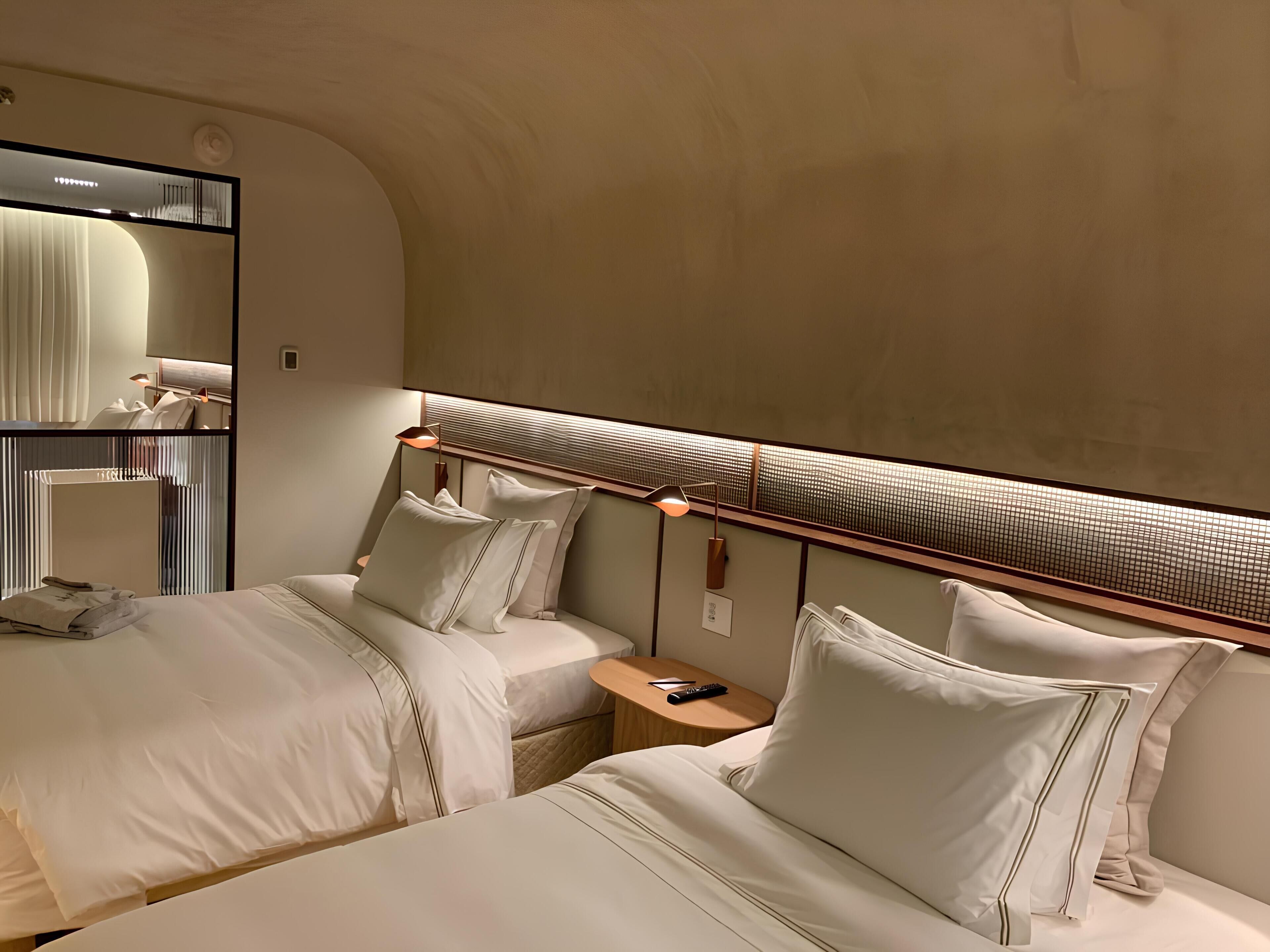 A hotel room with two beds, a large mirror, and a modern headboard with built-in lighting.