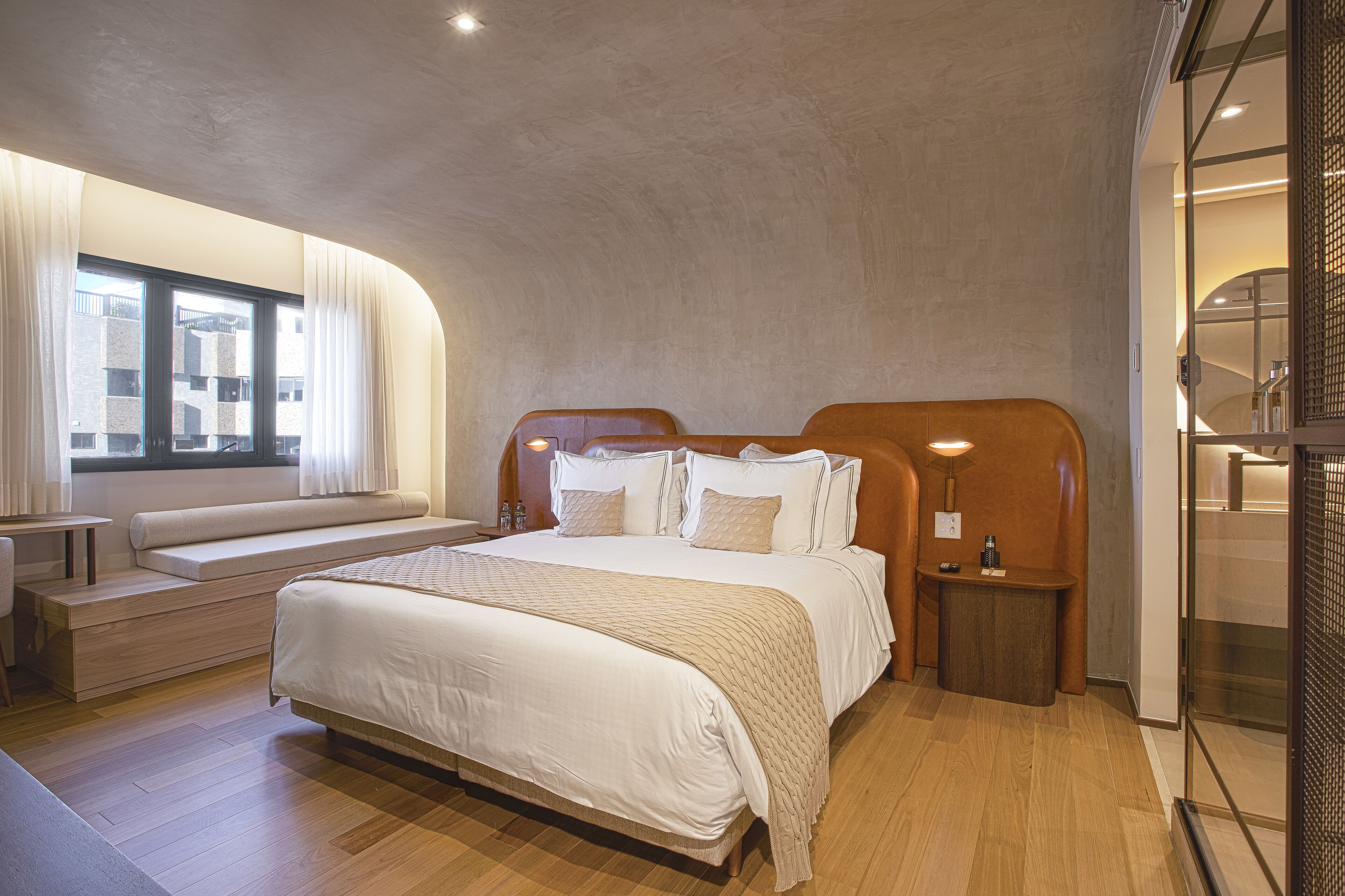 Quarto moderno com cama grande, assentos embutidos, mesa de cabeceira e vista para o exterior pela janela.