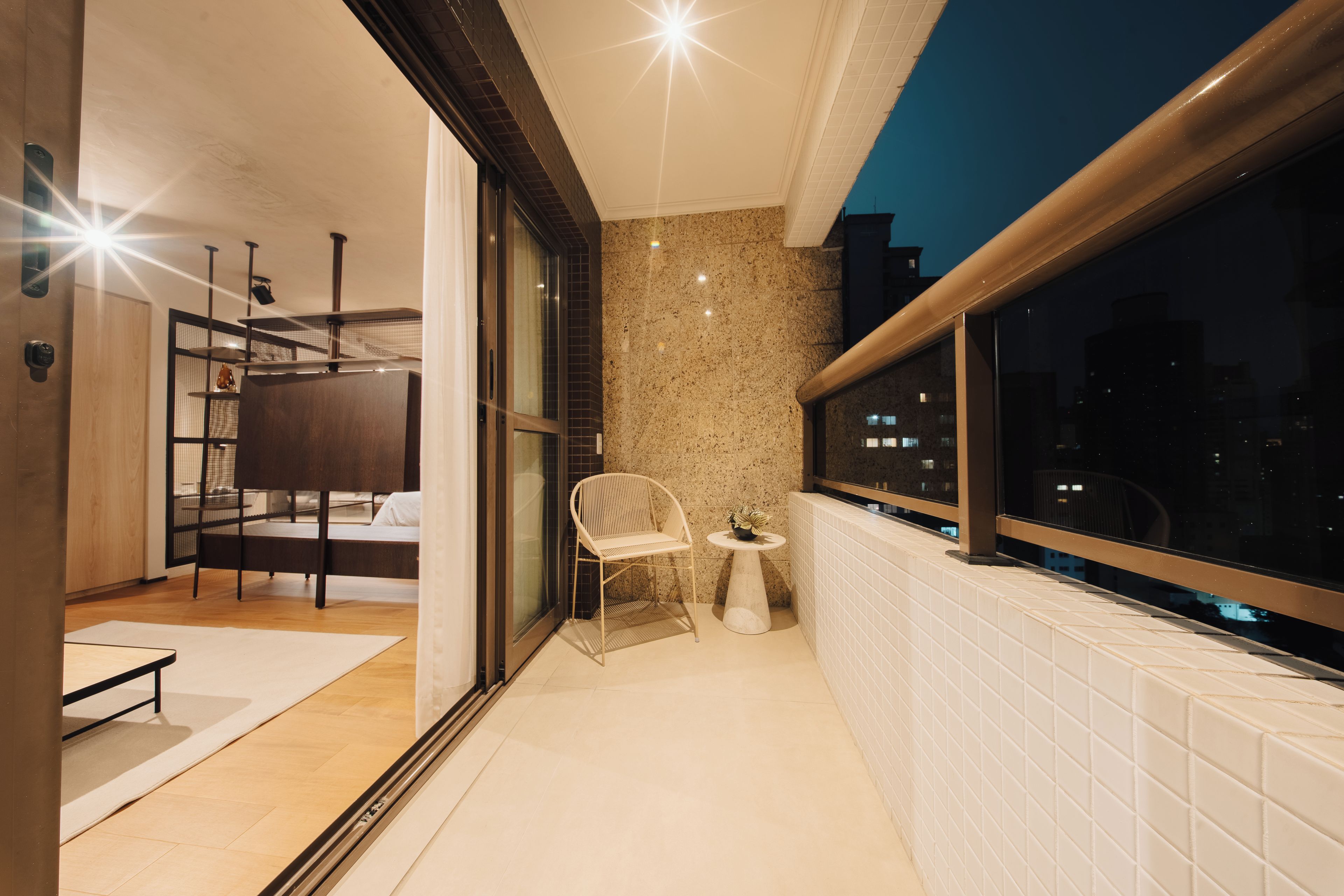 A modern balcony with a city view, a seating area with a chair and table, and a glass door leading to an interior space.
