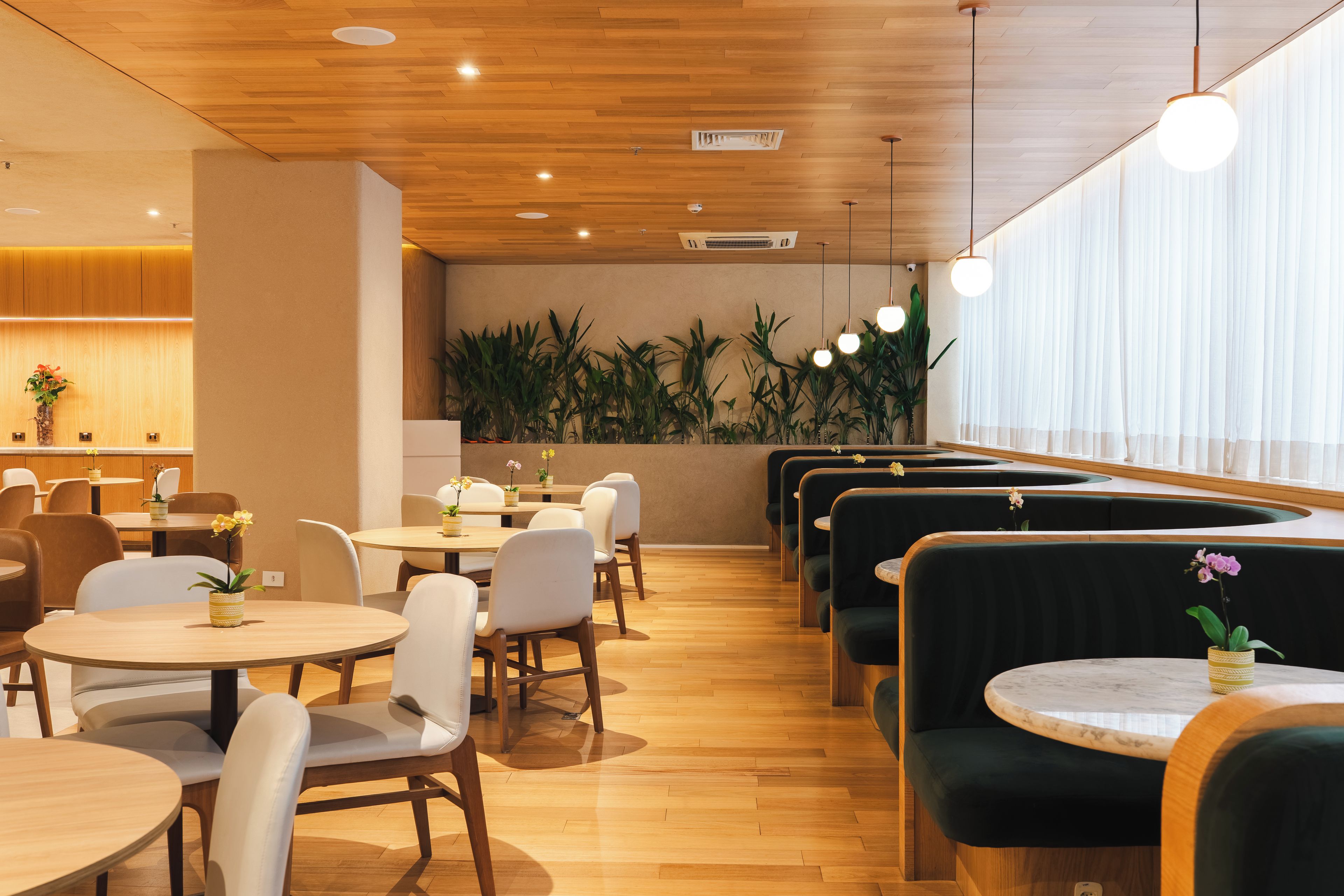 A modern dining area with wooden flooring, round tables, and booths.