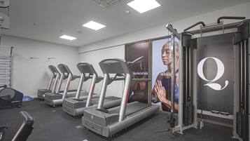 Une salle de sport équipée de tapis de course, d’appareils de musculation et d’un grand miroir.