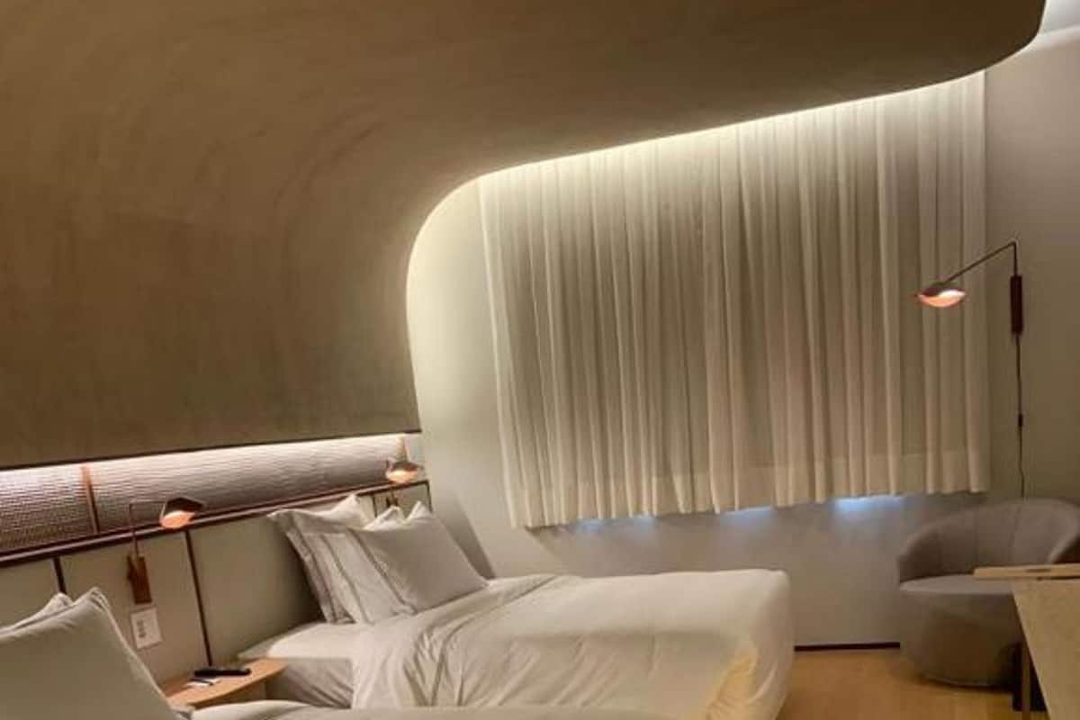 Ein modernes Hotelzimmer mit zwei Betten, einer Sitzecke und einem großen Fenster mit Vorhängen.