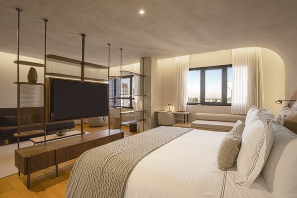 A modern hotel room with a large bed, a TV, a seating area, and a view of the city. - QOYA Hotel Curitiba, Curio Collection by Hilton (Curitiba)