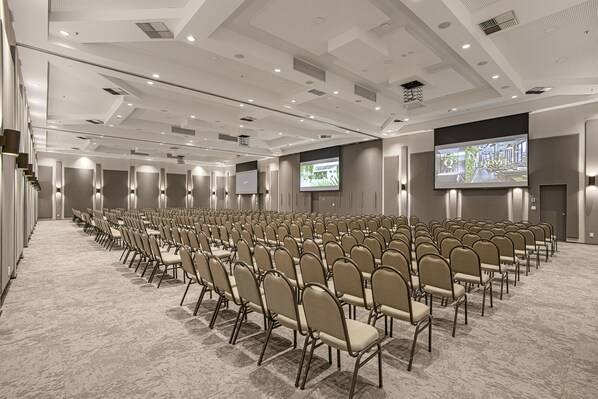 A conference room with rows of chairs, a large screen, and a projector. - QOYA Hotel Curitiba, Curio Collection by Hilton (Curitiba)