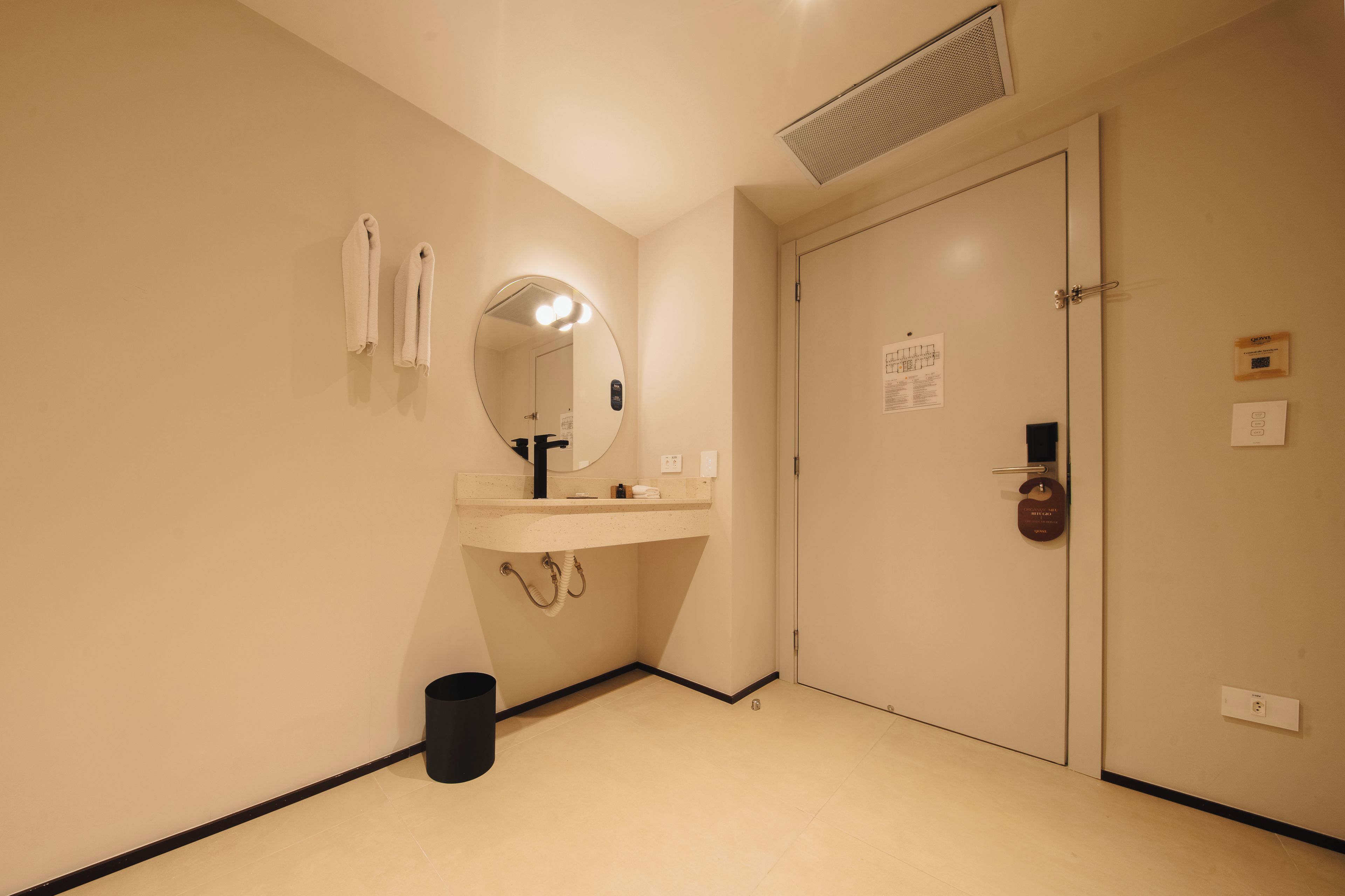 A hotel bathroom with a sink, mirror, towel rack, and a door with a lock.