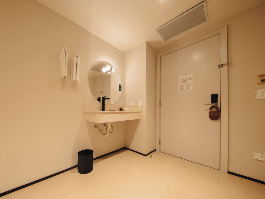 A hotel bathroom with a sink, mirror, towel rack, and a door with a lock.