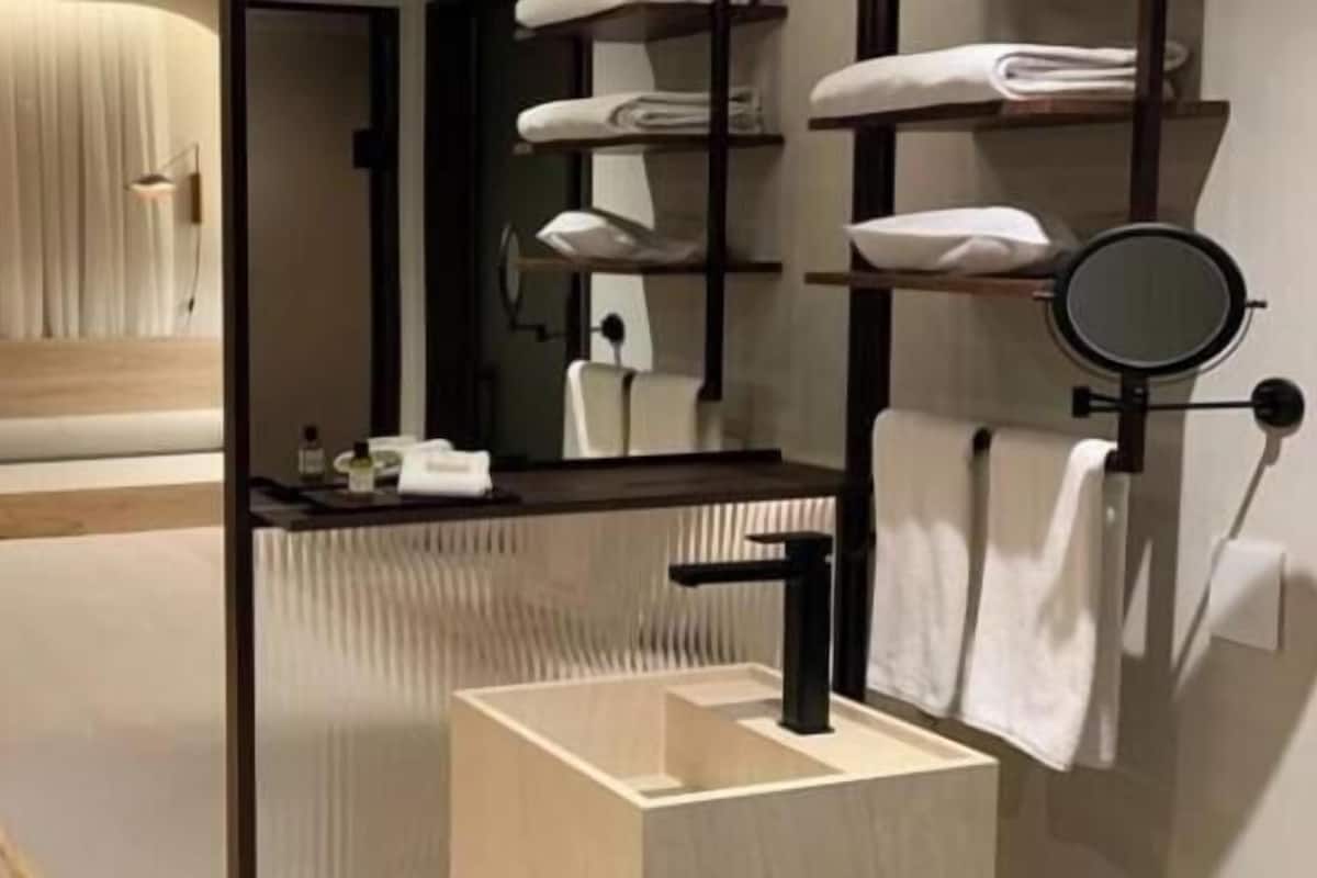 Ein modernes Hotelzimmer mit Bett, einer kleinen Sitzecke, einem Schreibtisch, einem runden Spiegel und einem integrierten Waschbecken.