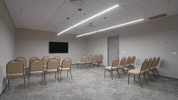 A conference room with beige chairs arranged in a semi-circle, a flat-screen TV mounted on the wall, and a carpeted floor.