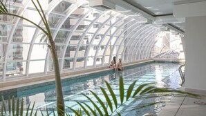 An indoor swimming pool with a glass ceiling, surrounded by palm trees. - QOYA Hotel Curitiba, Curio Collection by Hilton (Curitiba)