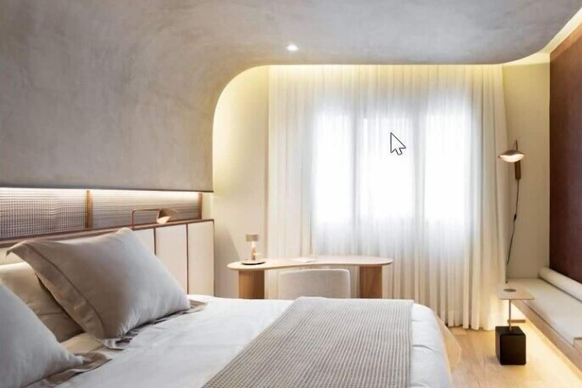 Une chambre d’hôtel moderne équipée d’un lit, d’un bureau, d’une chaise, d’une lampe et d’un grand miroir.