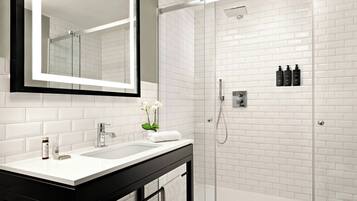 Un baño moderno con ducha de azulejos blancos, un espejo grande y un tocador negro.