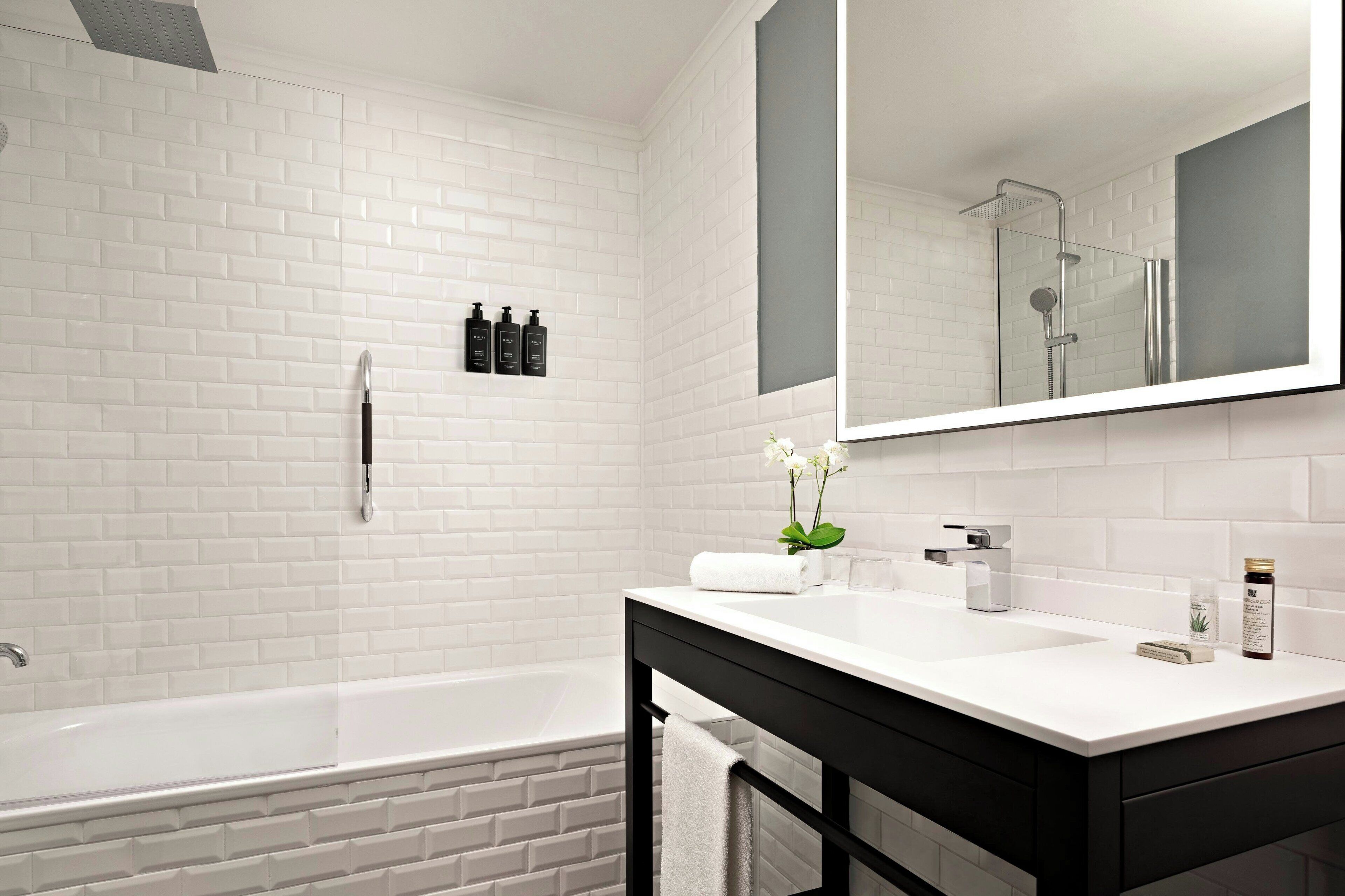 A modern bathroom with white brick walls, a white bathtub, a large mirror, and a black vanity with a sink.