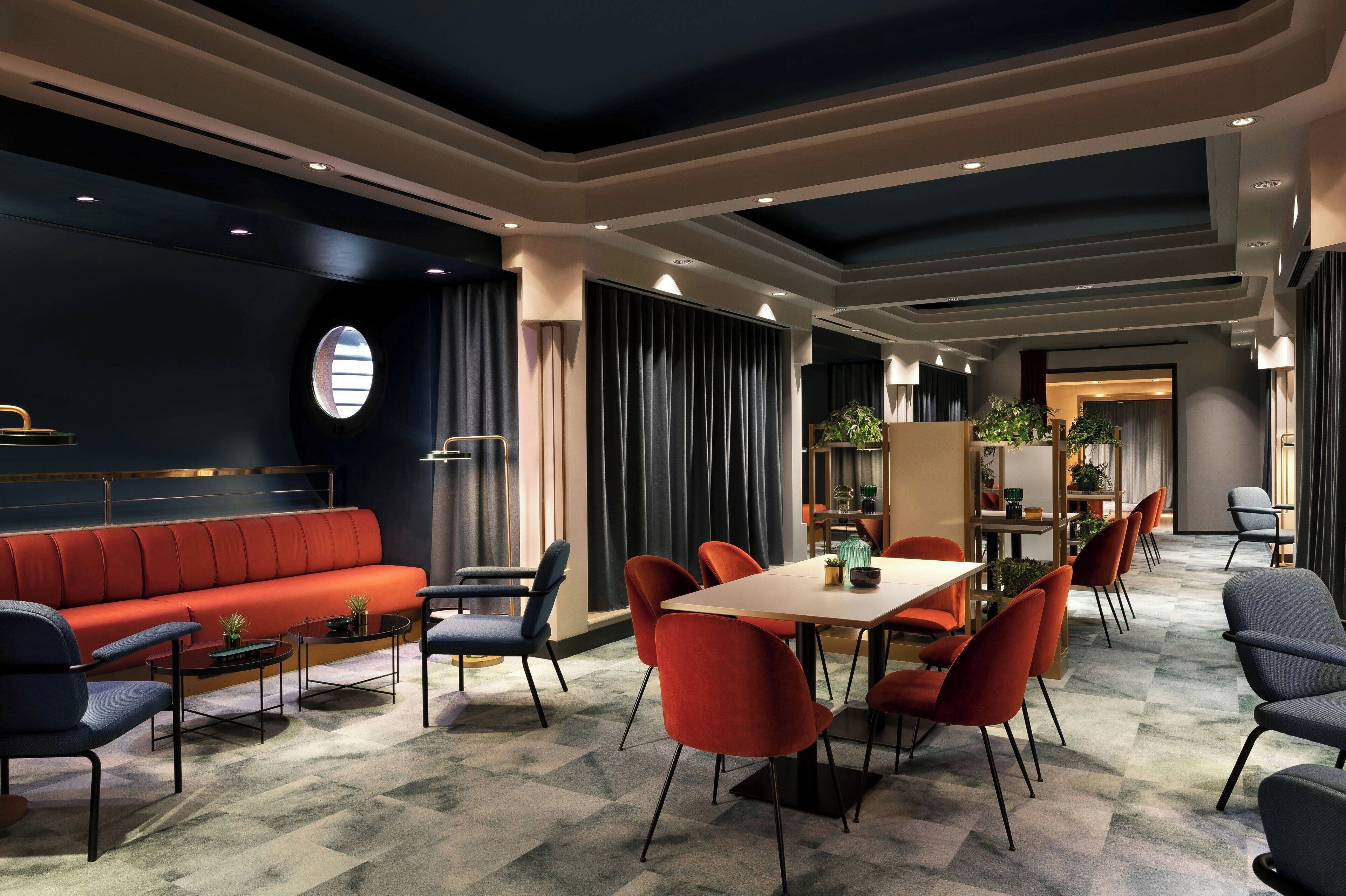 Un hall d’hôtel moderne avec un canapé rouge, des tables rondes et des chaises rouges et grises.