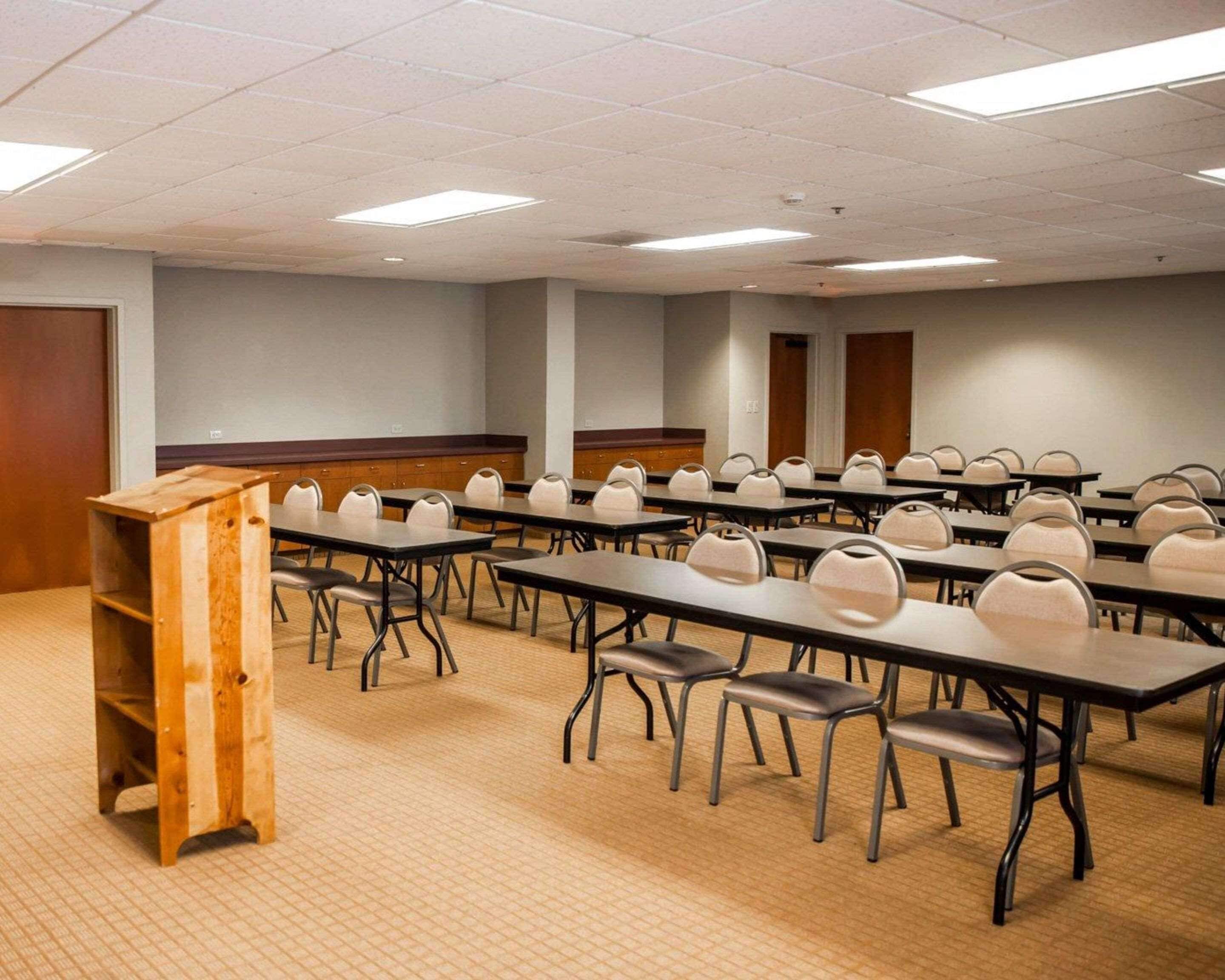 A conference room with multiple tables and chairs, a podium, and a carpeted floor.
