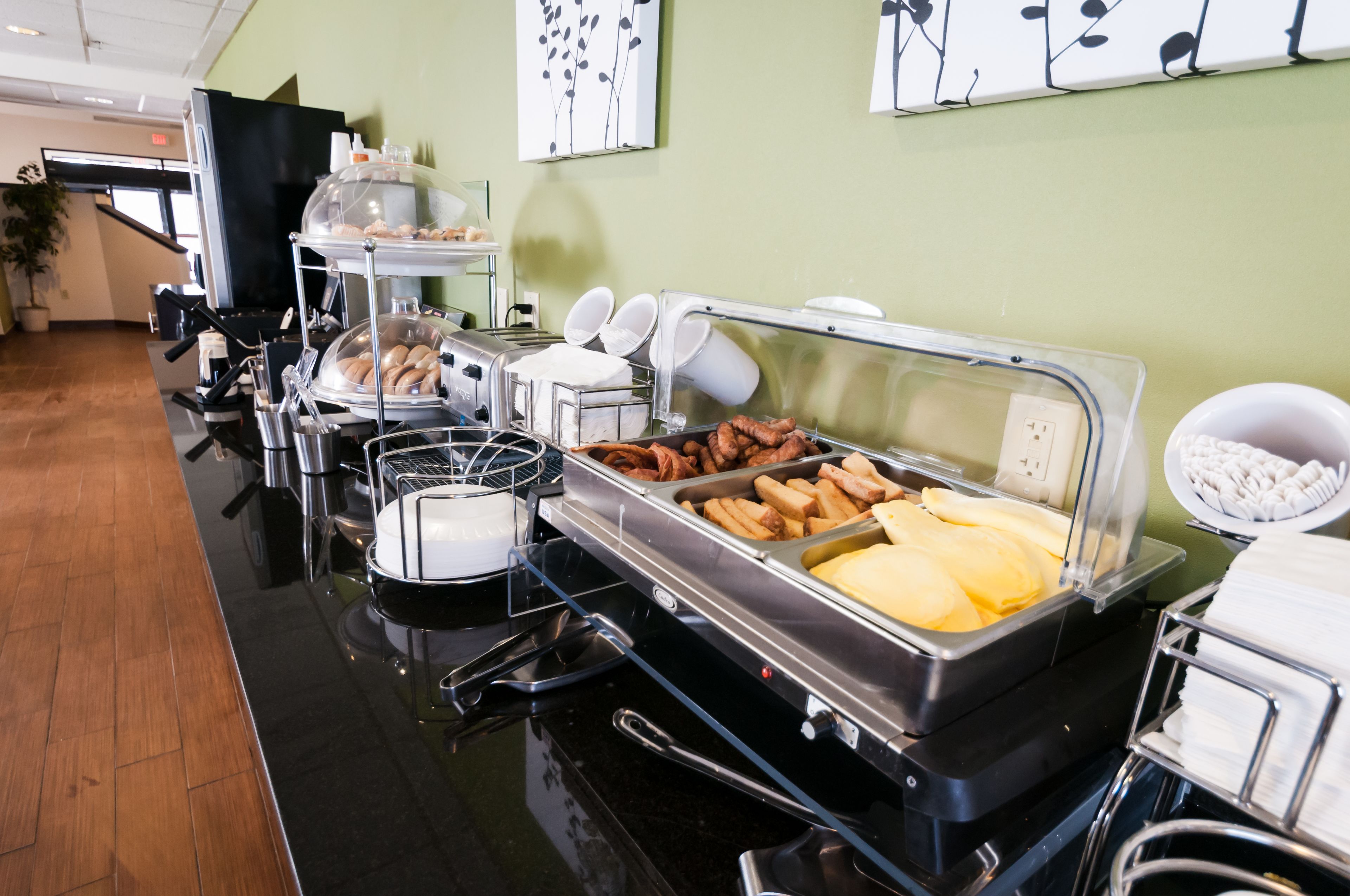 A buffet with various food items, including pastries, fruits, and meats, in a modern setting with green walls and a wooden floor.