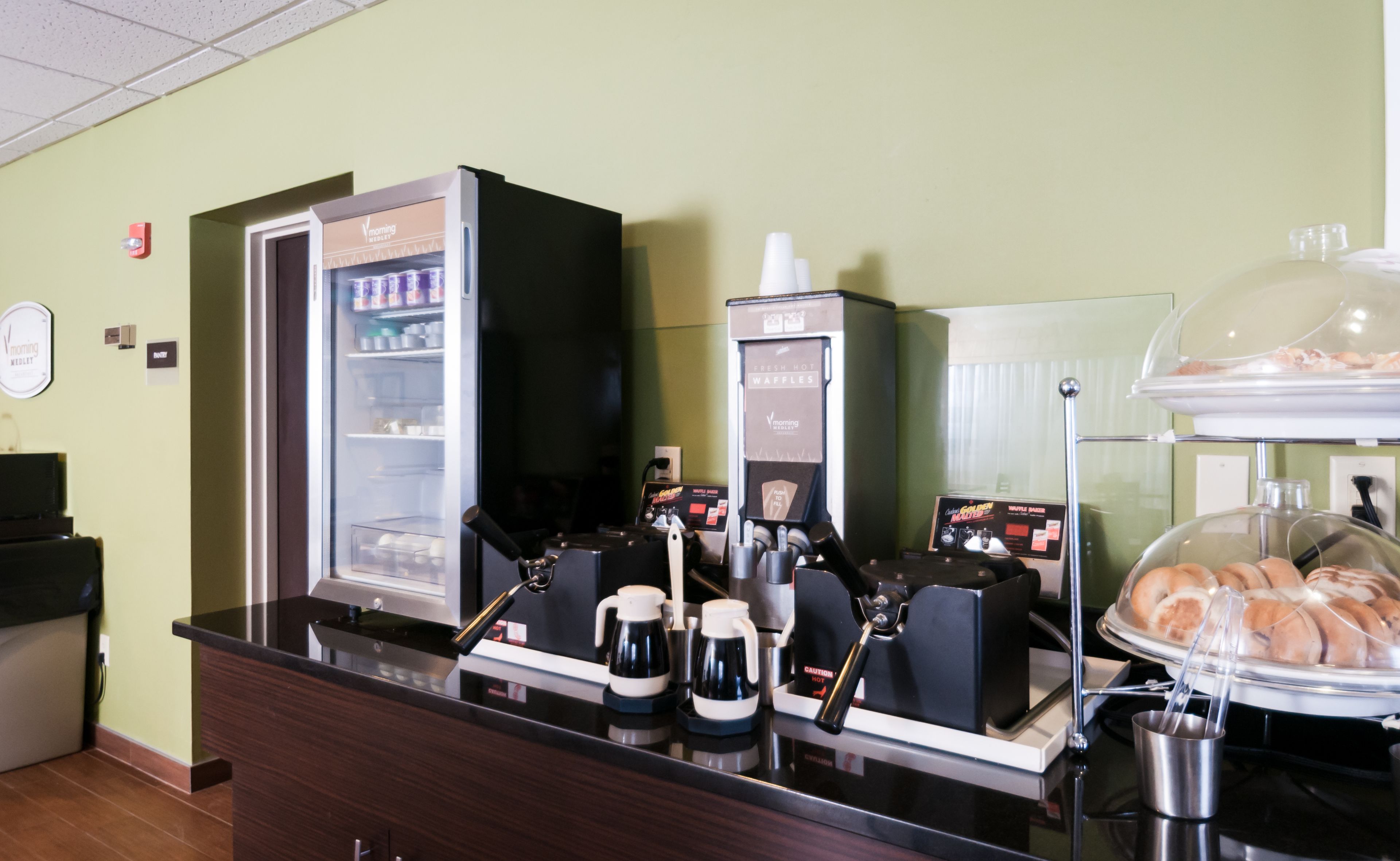 A coffee station with a coffee machine, a waffle maker, and a display case with waffles.