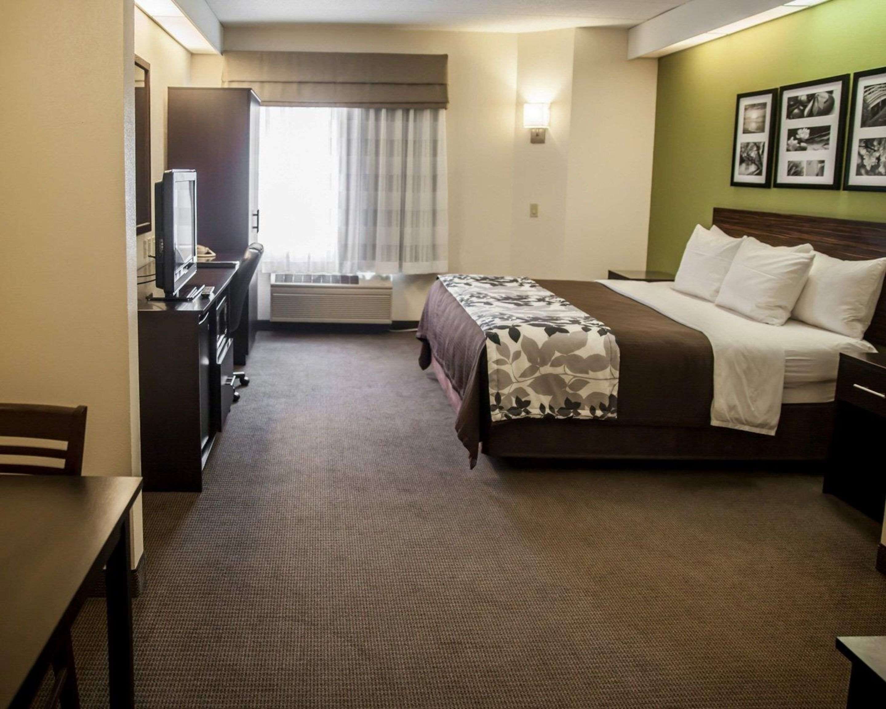 Una habitación de hotel con cama, escritorio, silla, televisor y ventana con cortinas.
