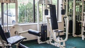 Une salle de sport équipée de divers appareils d’exercice, dotée d’un sol recouvert d’une moquette verte et offrant une vue sur une voiture et la verdure à l’extérieur.