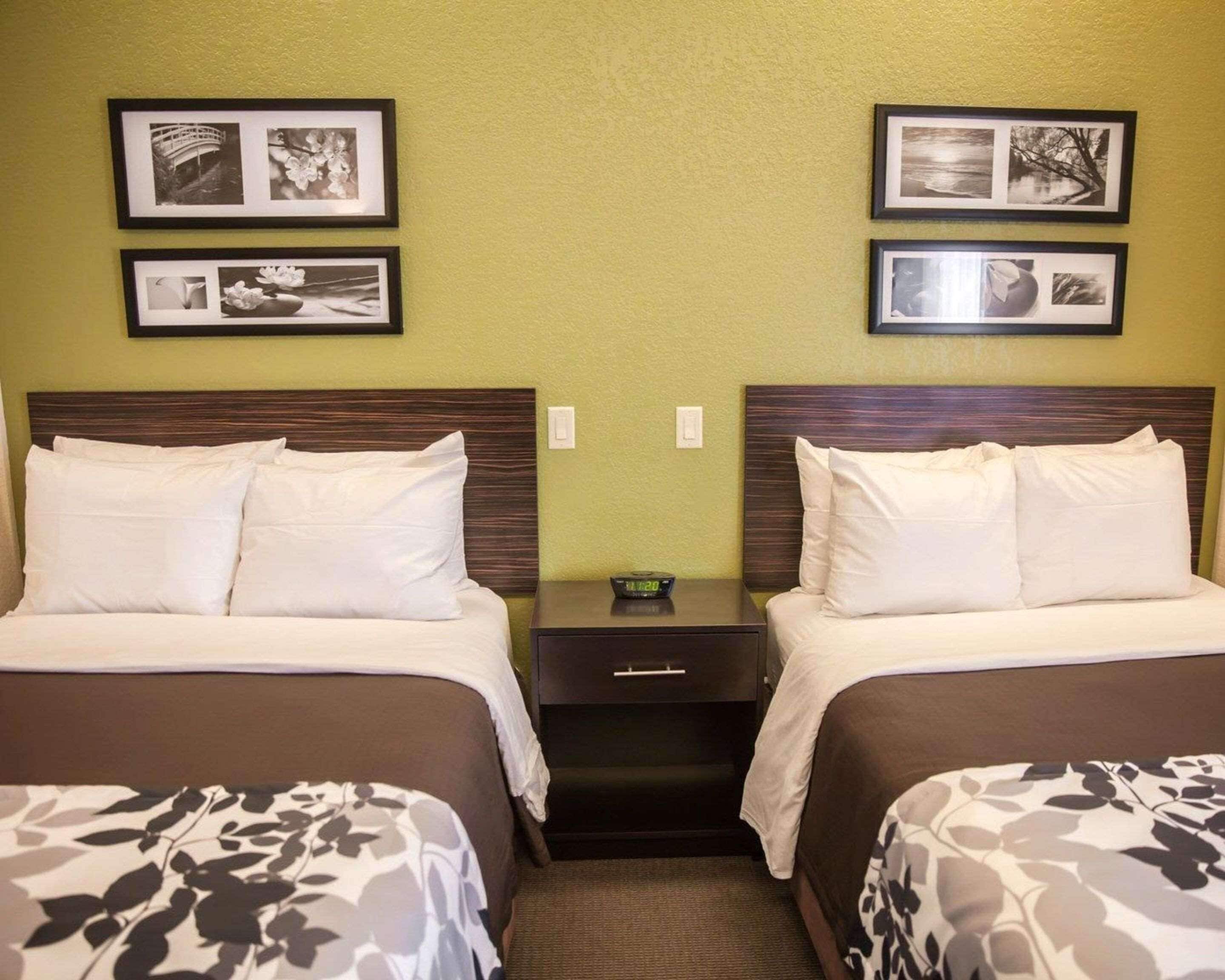 A hotel room with two beds, a nightstand with a clock, and framed pictures on the wall.