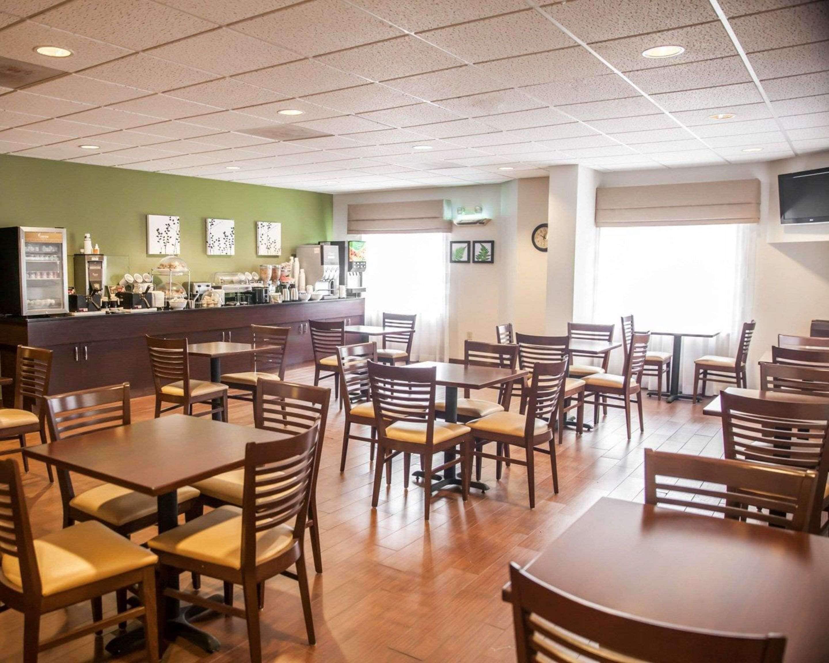 Uma ampla área de refeições com mesas e cadeiras de madeira, um espaço para café e uma parede verde decorativa.