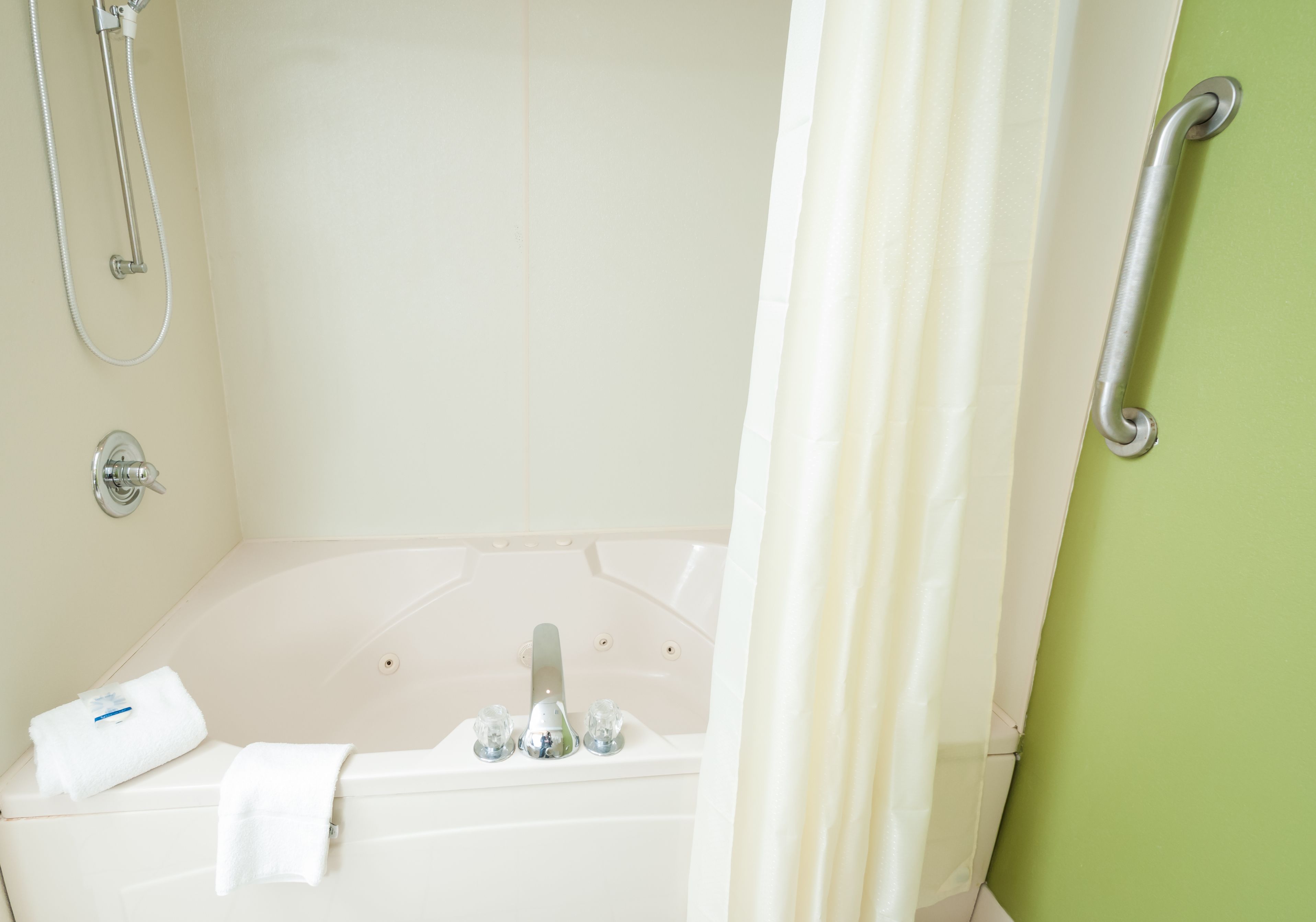 Une salle de bain équipée d’une baignoire, d’une pomme de douche, d’une serviette et d’une barre d’appui.