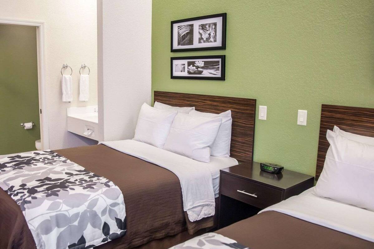 A hotel room with two beds, a nightstand, a digital clock, and framed pictures on the wall.
