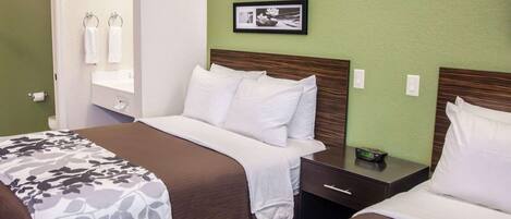A hotel room with two beds, a nightstand, a digital clock, and framed pictures on the wall.