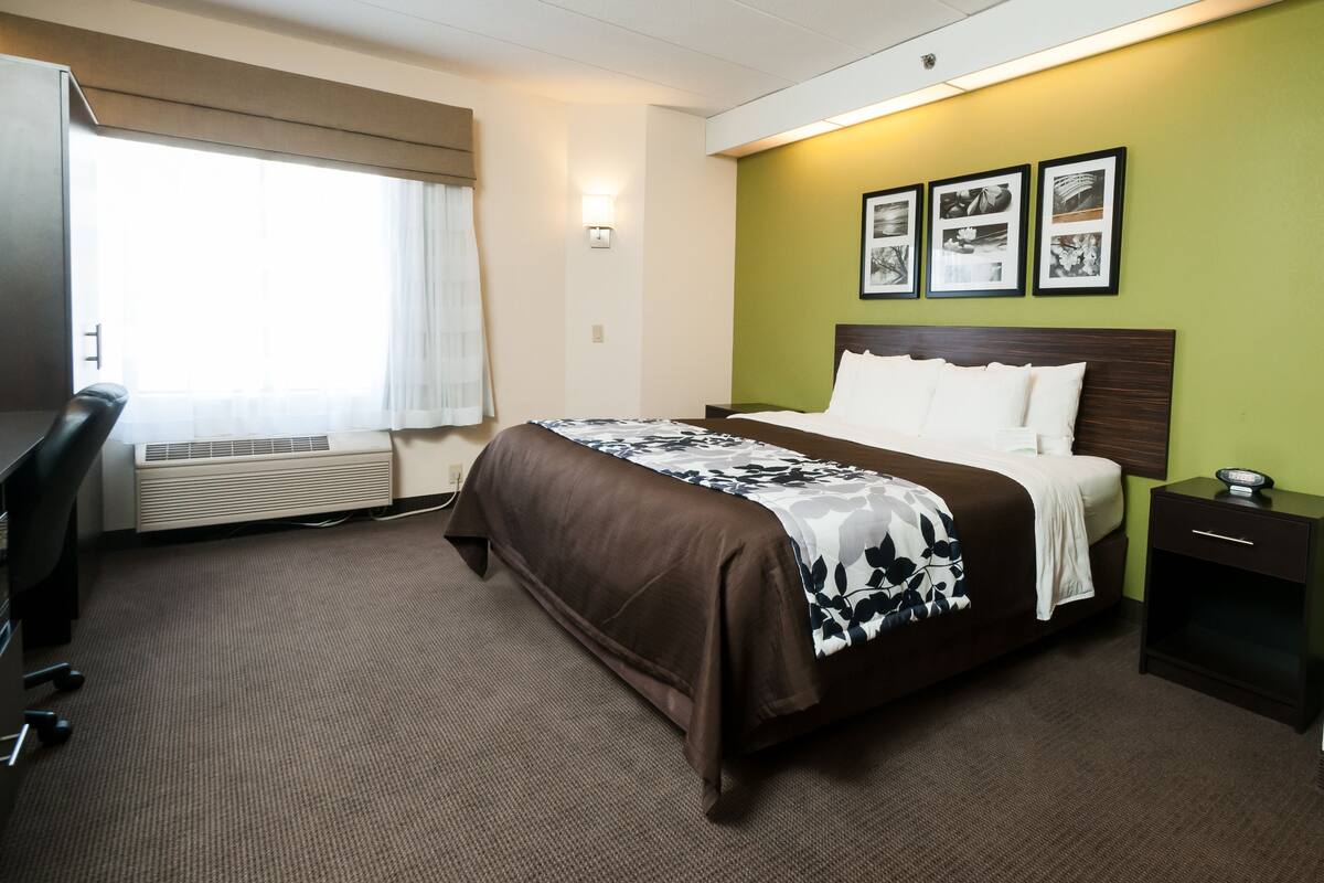 A hotel room with a bed, a desk, and a chair. There are three framed pictures on the wall.
