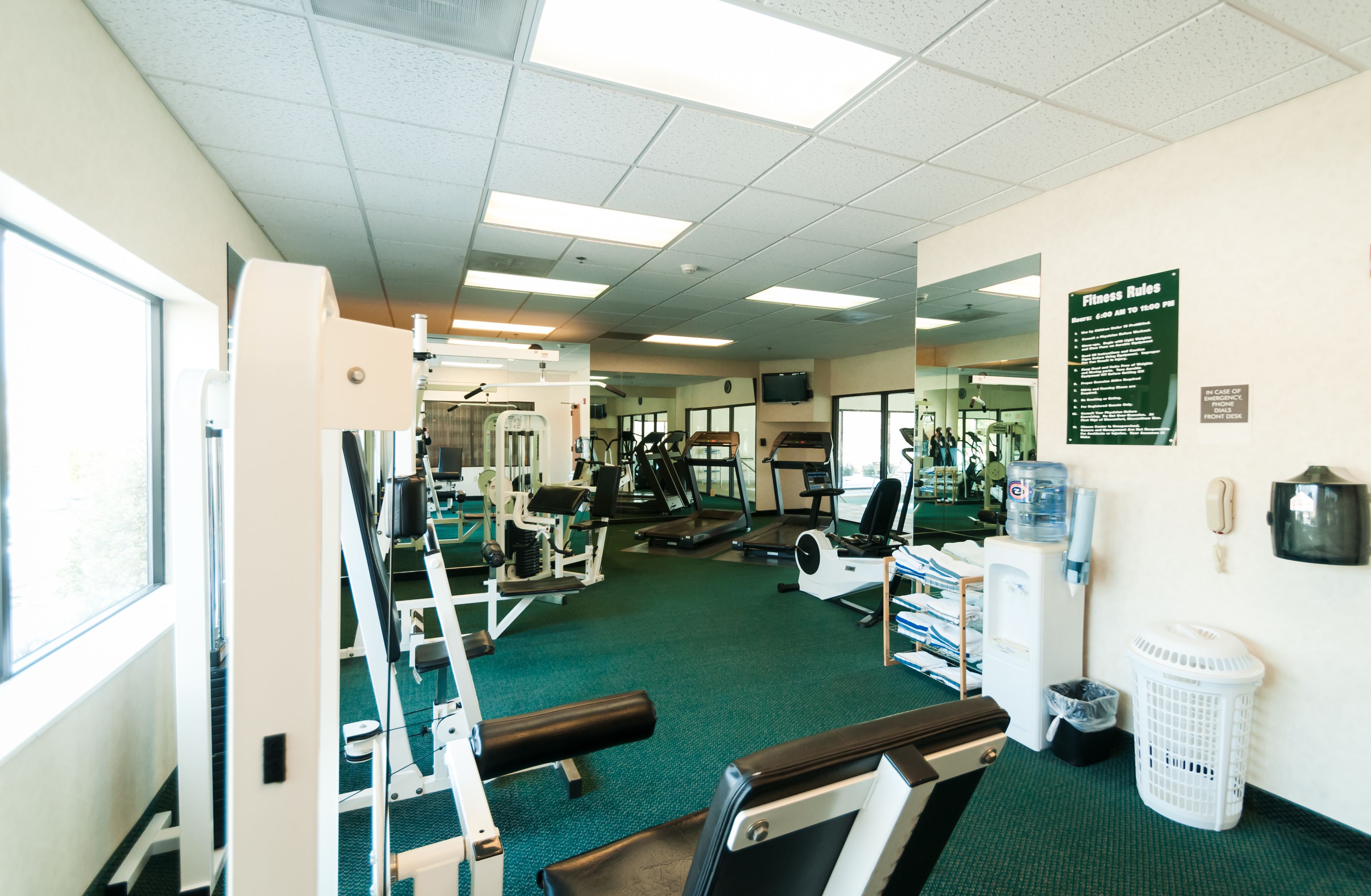 A gym with various exercise equipment, a water dispenser, and a sign with fitness rules.