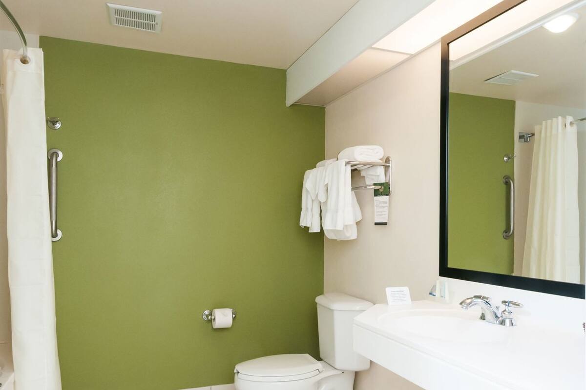 A bathroom with a green wall, white fixtures, a toilet, a sink with a mirror, and a shower curtain.