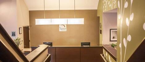 A reception area with a desk, a sign for Sleep Inn & Suites, a welcome mat, and a staircase.