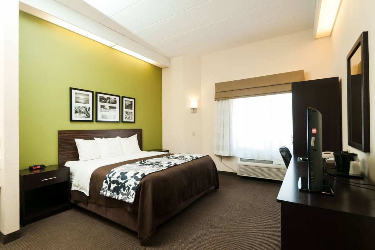 A hotel room with a bed, a desk, a television, and a window with curtains.
